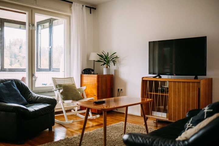 Pieni olohuone, jossa sohva, sohvapöytä, nojatuoli, keinutuoli ja piirongin päällä oleva televisio