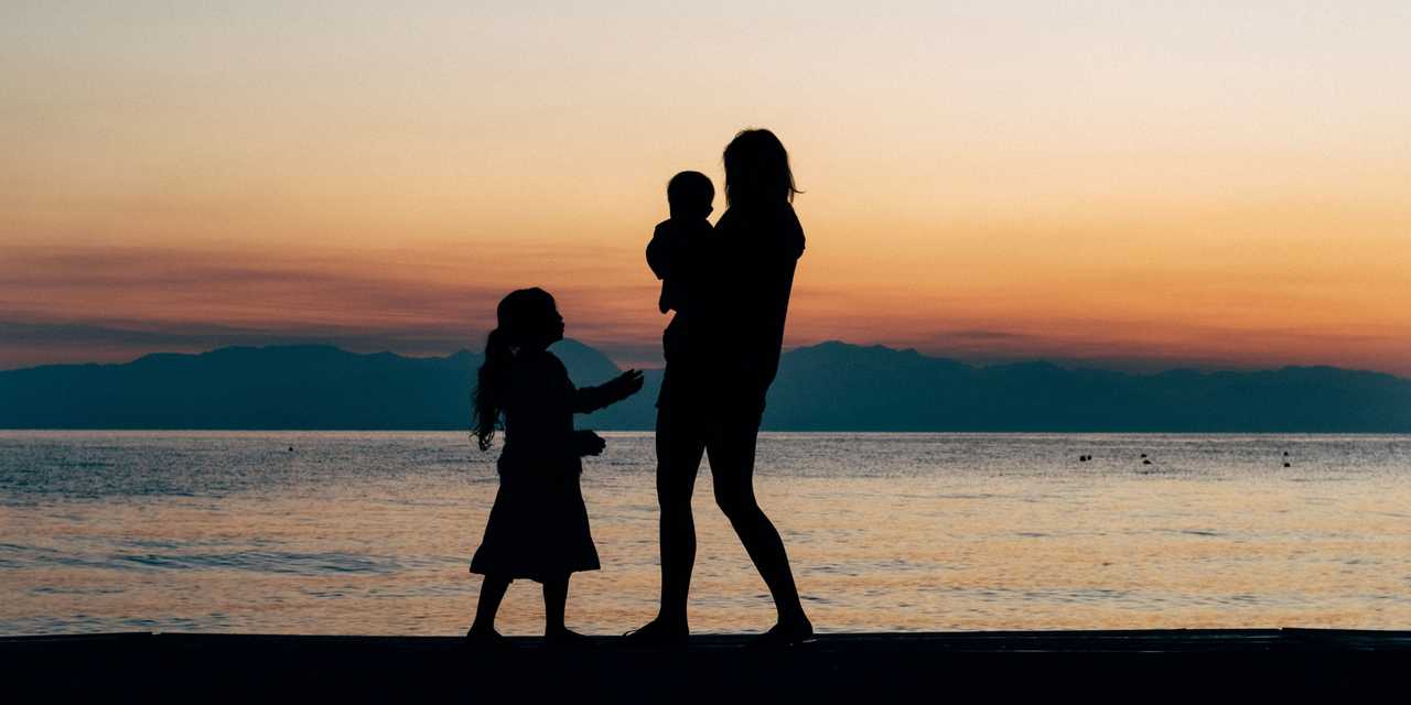 Nainen ja kaksi lasta rannalla auringonlaskussa