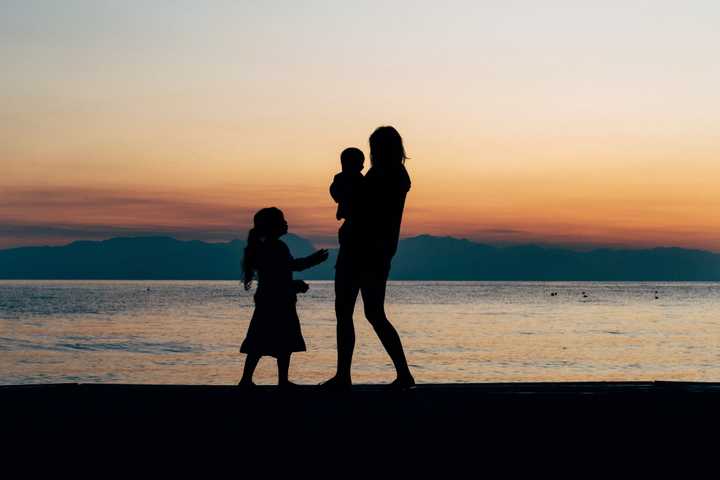 Nainen ja kaksi lasta rannalla auringonlaskussa