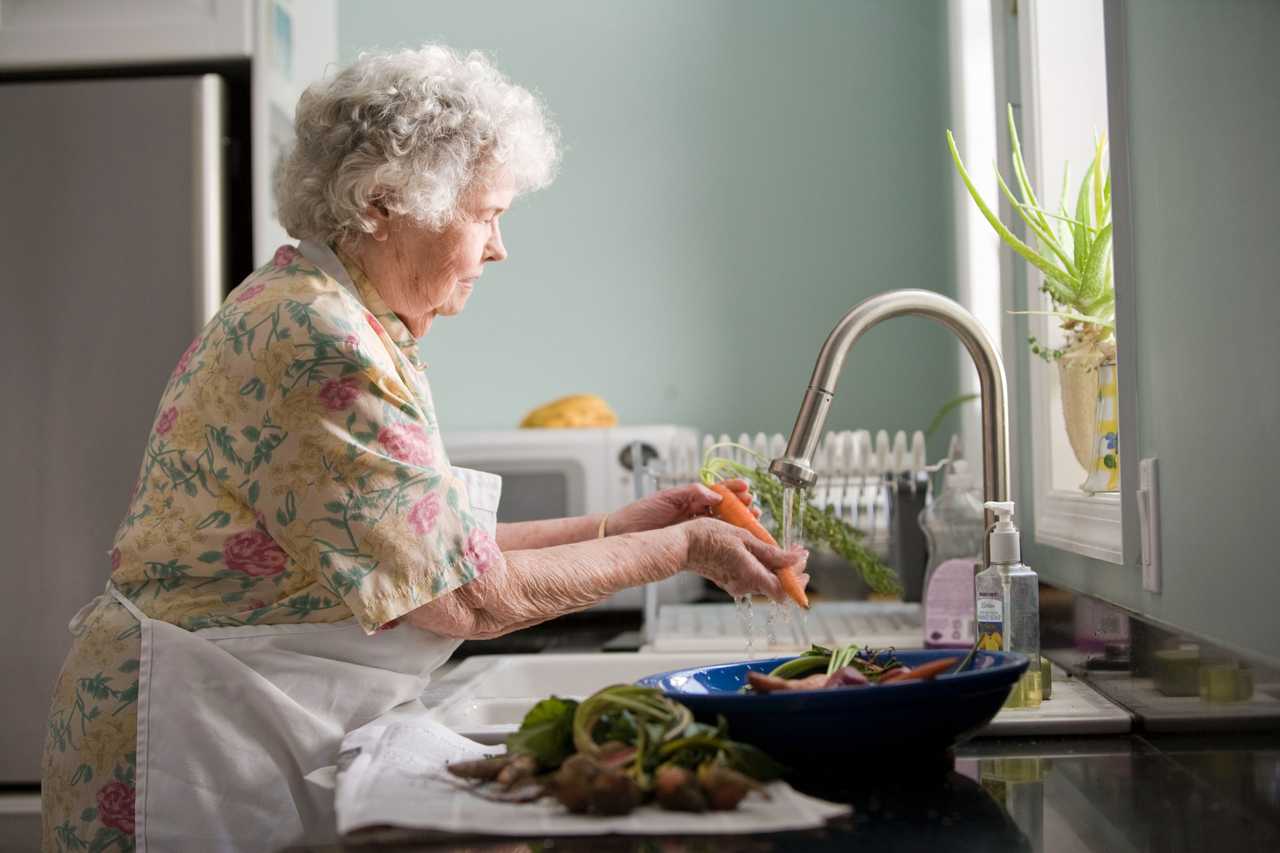 vanhempi henkilö pesemässä vihanneksia.