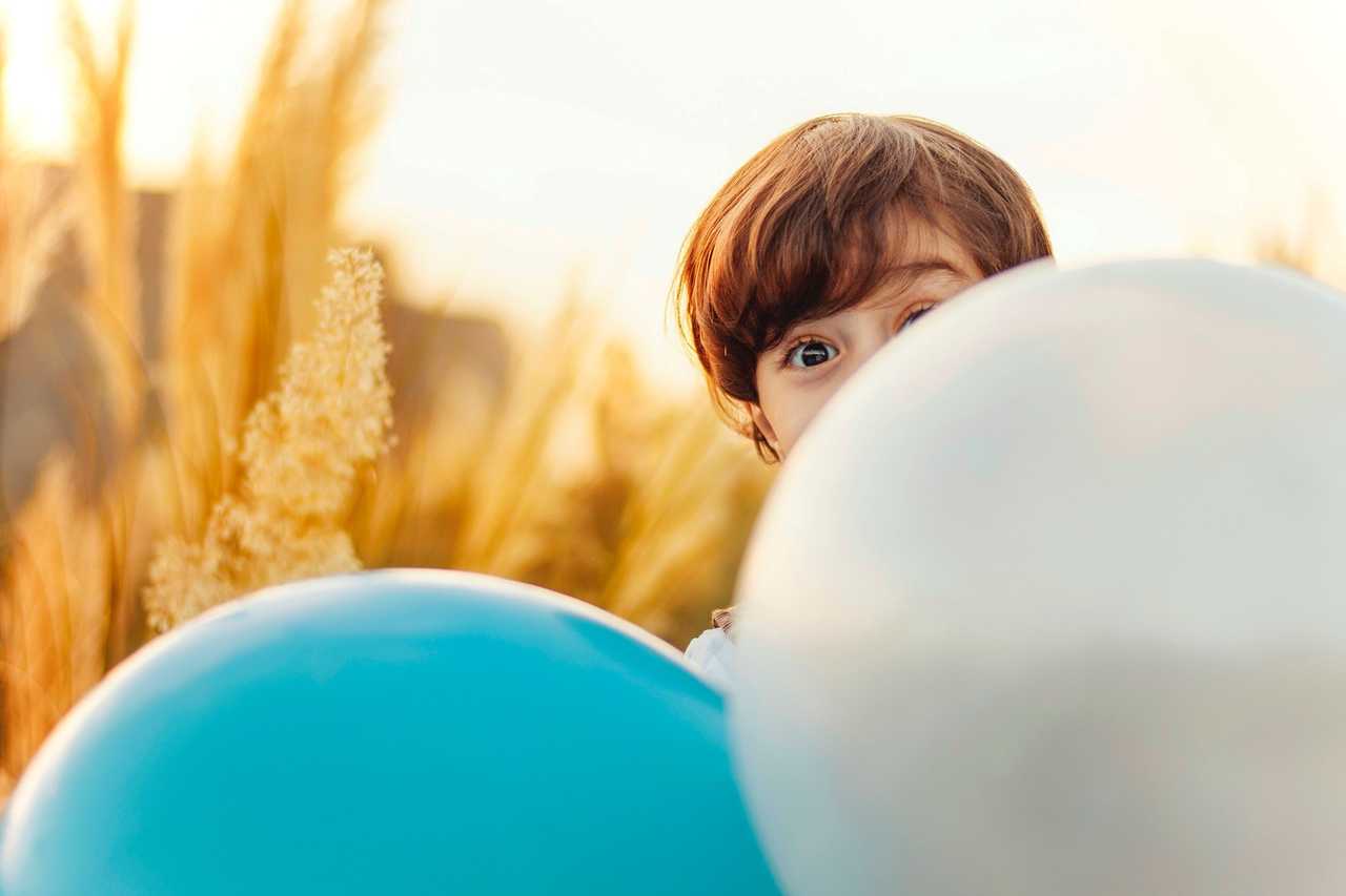 Pojke gömmer sig bakom två ballonger