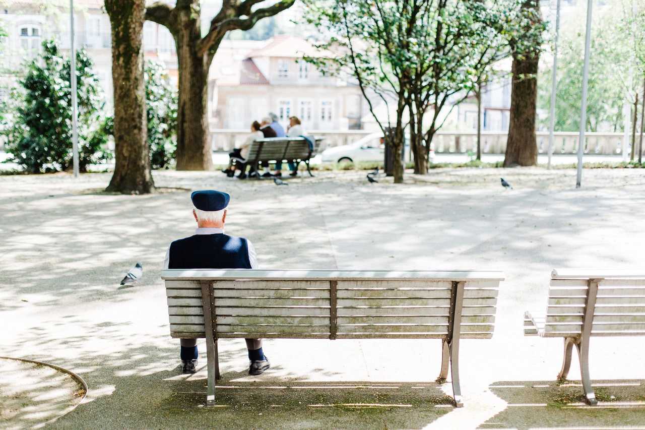 Man som sitter på bänk i en solig plats