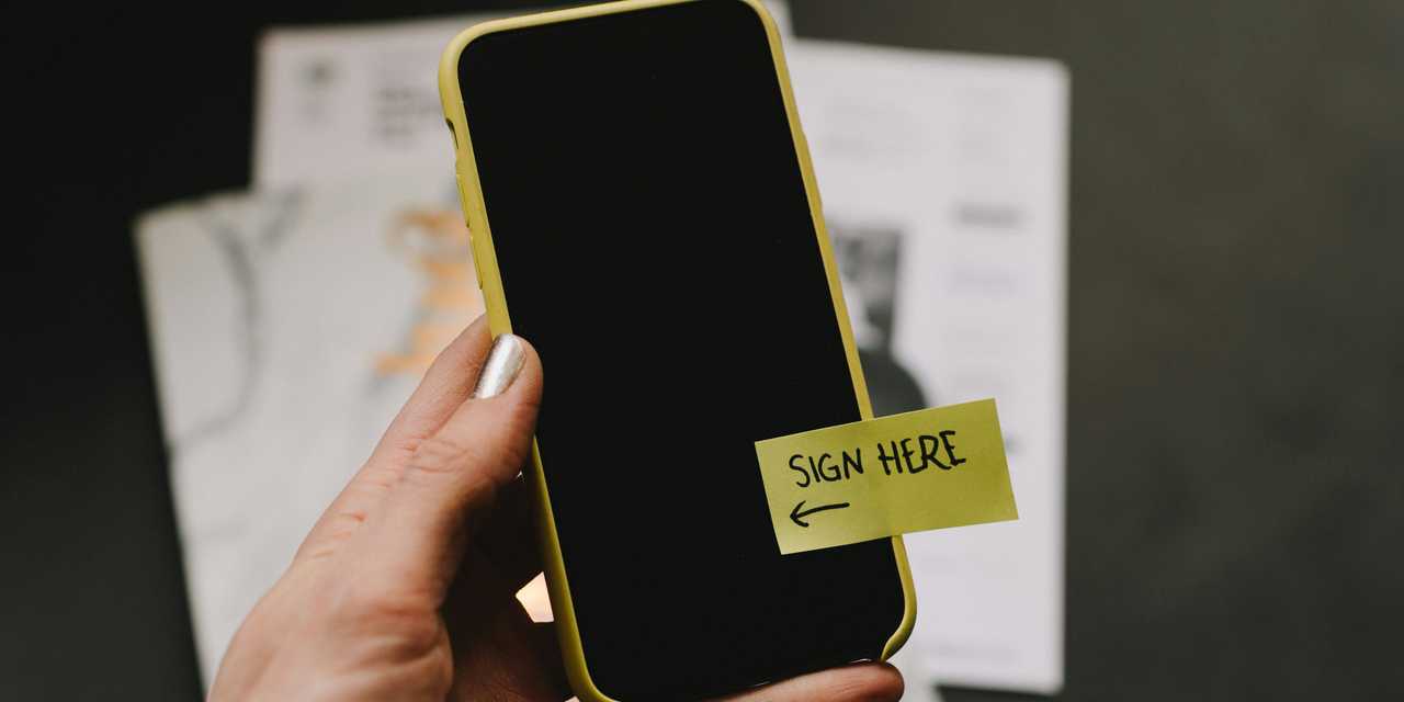 A person holding a smartphone where is a sticky tape saying "Sign here".