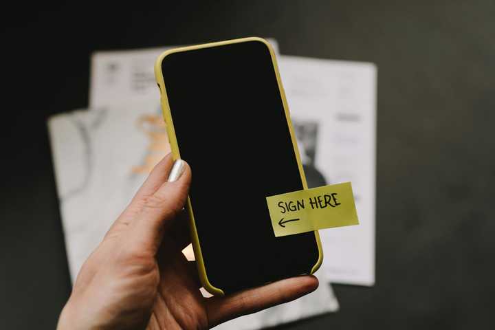A person holding a smartphone where is a sticky tape saying "Sign here".