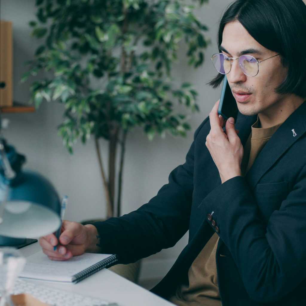 A person holding a phone and writing to a notepad