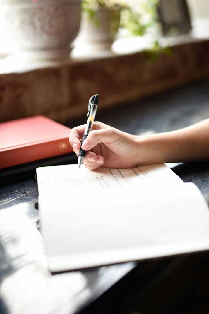A person writing with a pen to a notebook