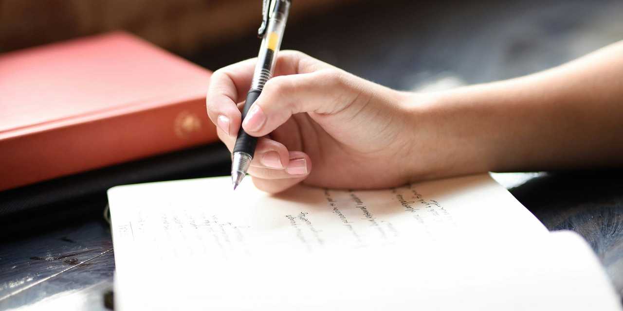 A person writing with a pen to a notebook