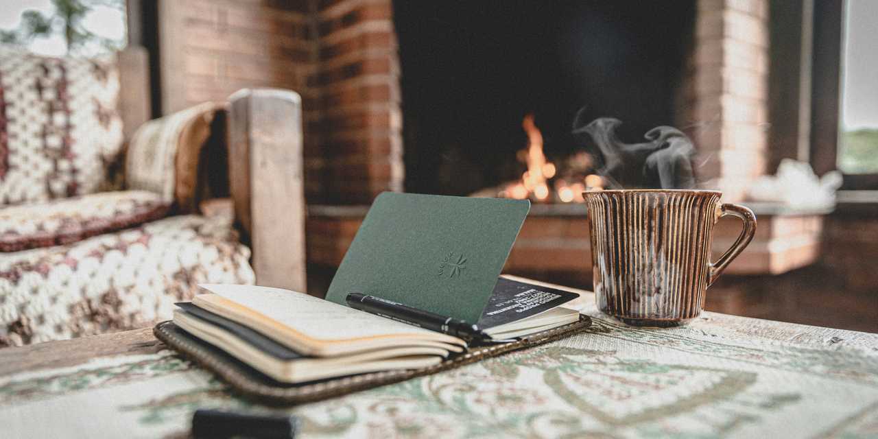 A Notebook on a coffee table and fireplace lit on the background