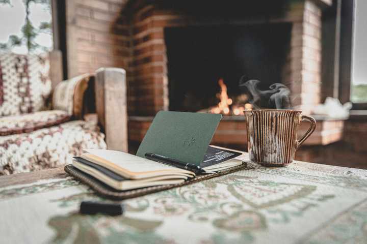 A Notebook on a coffee table and fireplace lit on the background