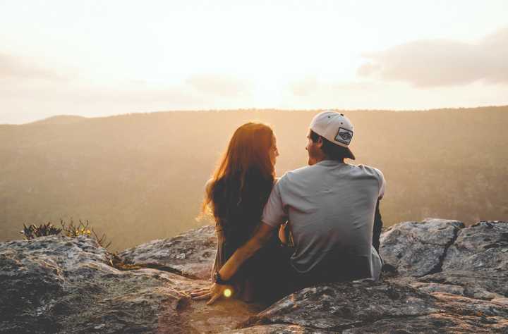 Pariskunta istuu kalliolla ja katsoo auringonlaskua