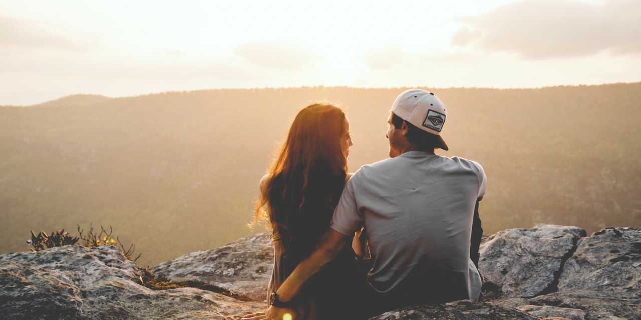 Pariskunta istuu kalliolla ja katsoo auringonlaskua