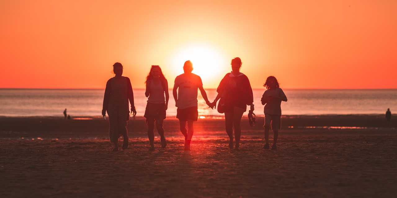 Perhe kävelee rannalla kohti auringonlaskua