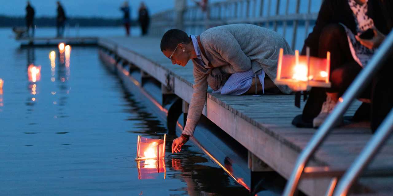 People placing a candle on water from a dock