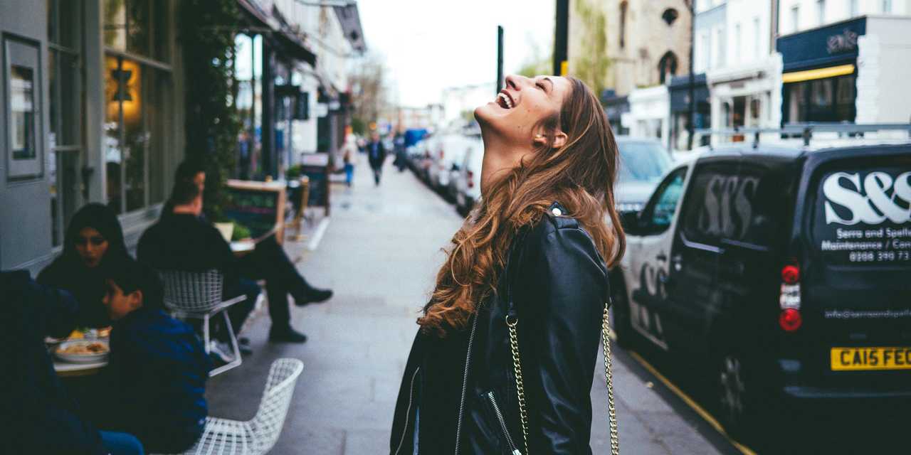 A Woman in leather jacket laughing on a London street.