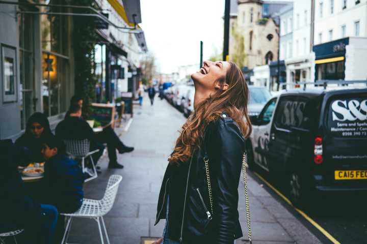 A Woman in leather jacket laughing on a London street.