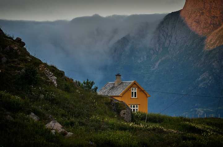 Keltainen talo maaseudulla. Vuoria taustalla. 