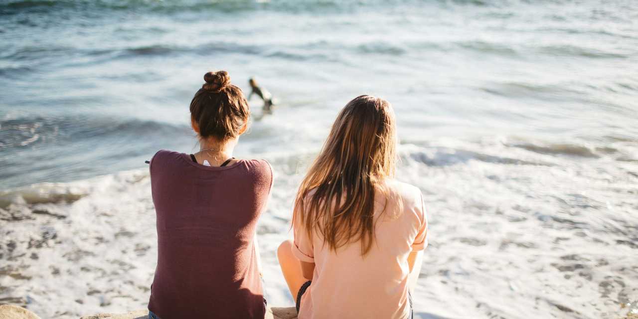 Kaksi ystävää istuu meren rannalla