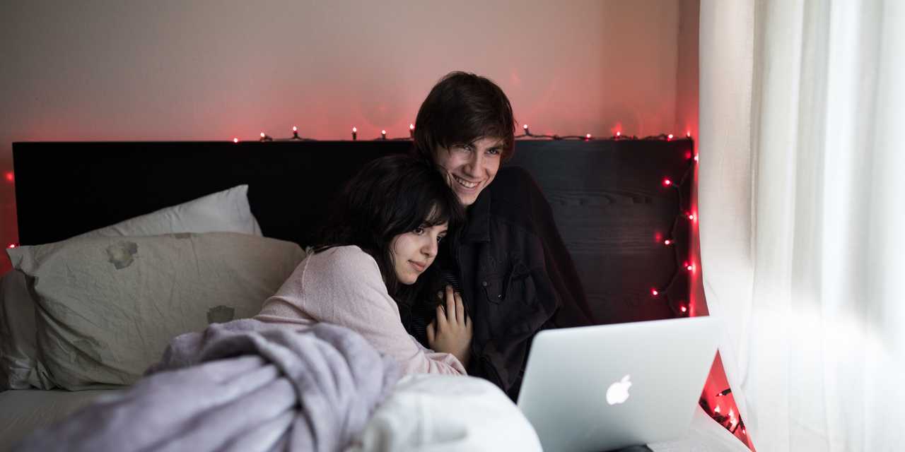 Pariskunta makaa sängyllä ja katsoo kannettavaa tietokonetta