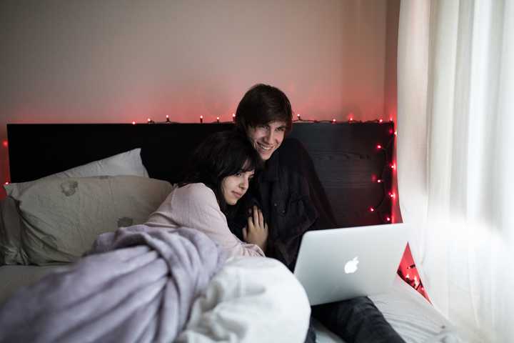 Pariskunta makaa sängyllä ja katsoo kannettavaa tietokonetta
