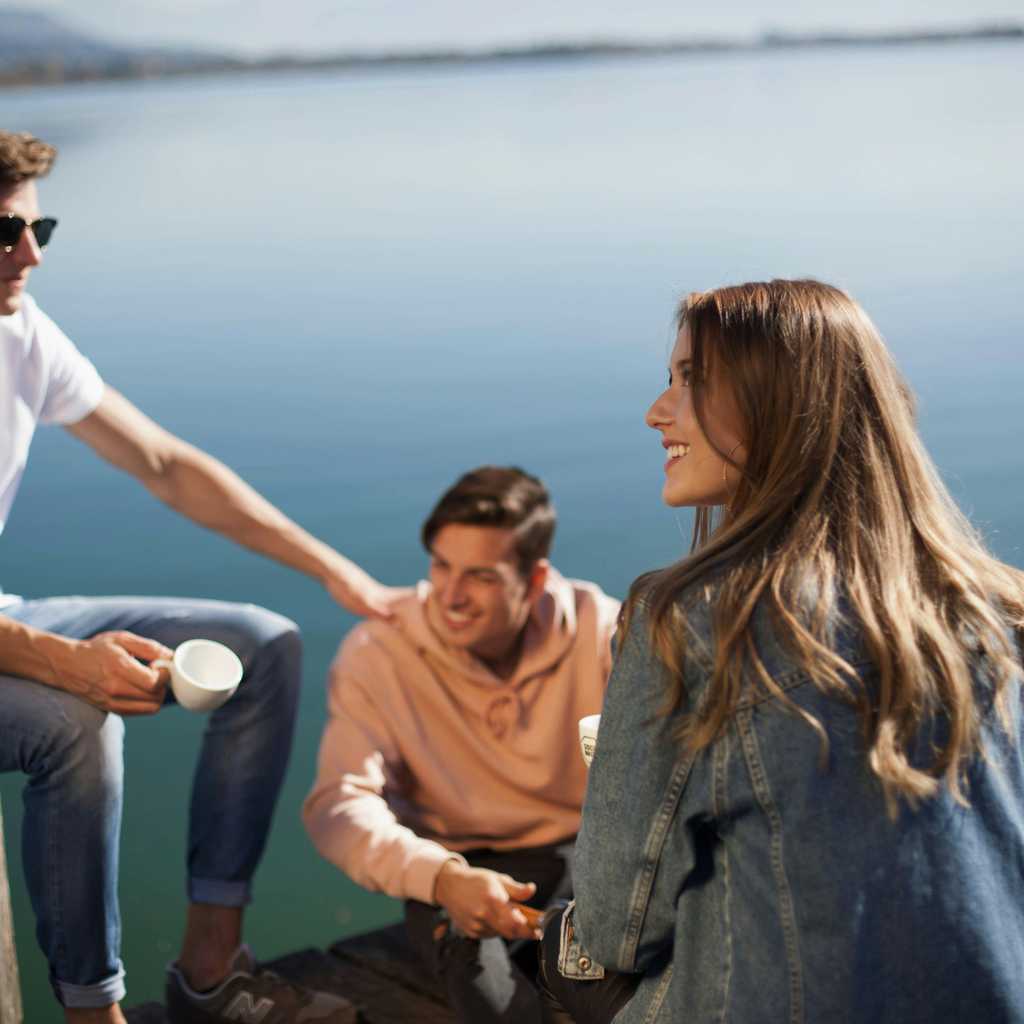 Friends sitting on pier and drinking coffee.