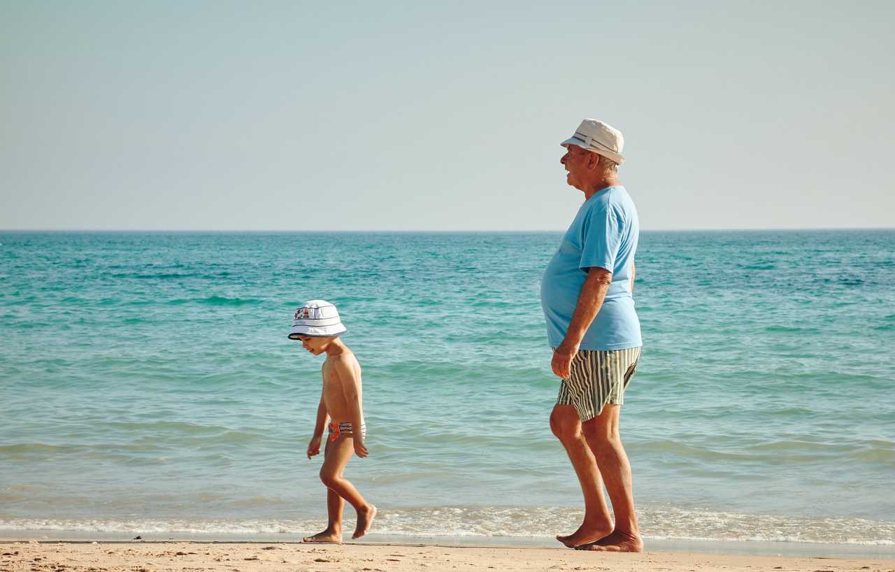 Farfar eller morfar på stranden med ett barn.