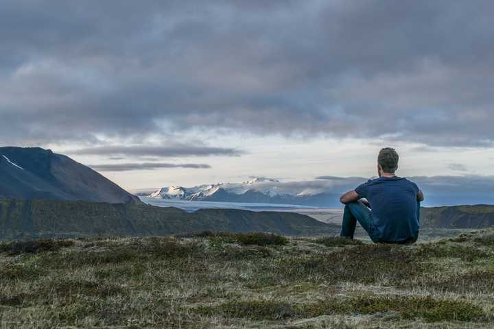 Henkilö istuu maassa, taustalla vuoria