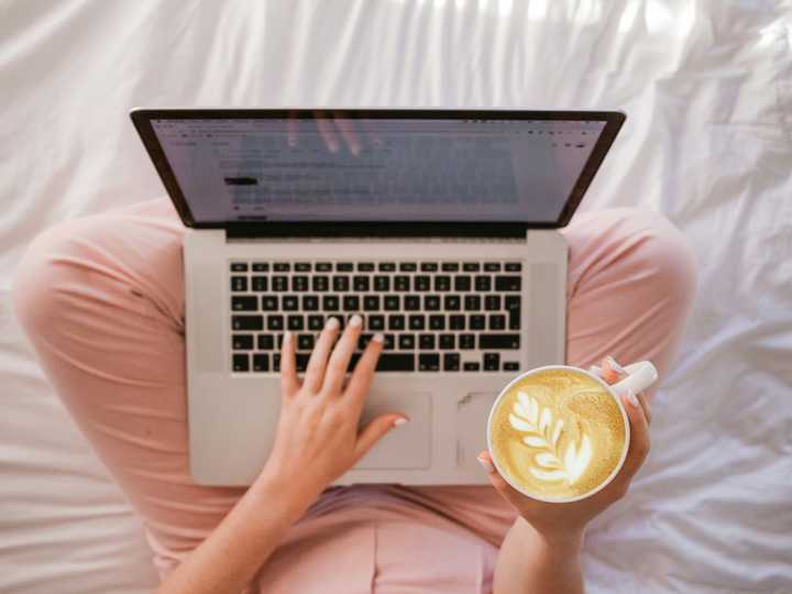Using a laptop in bed and drinking cappuccino 
