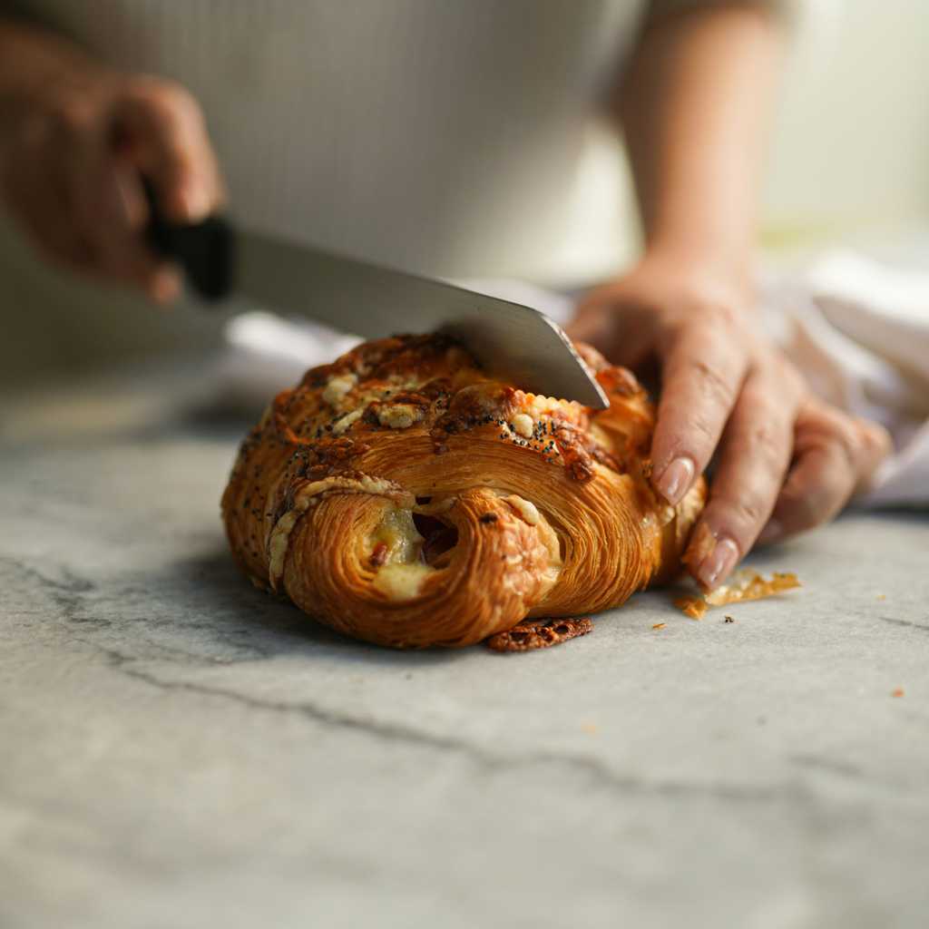 A bakery chef cutting a pastry with a bread knife