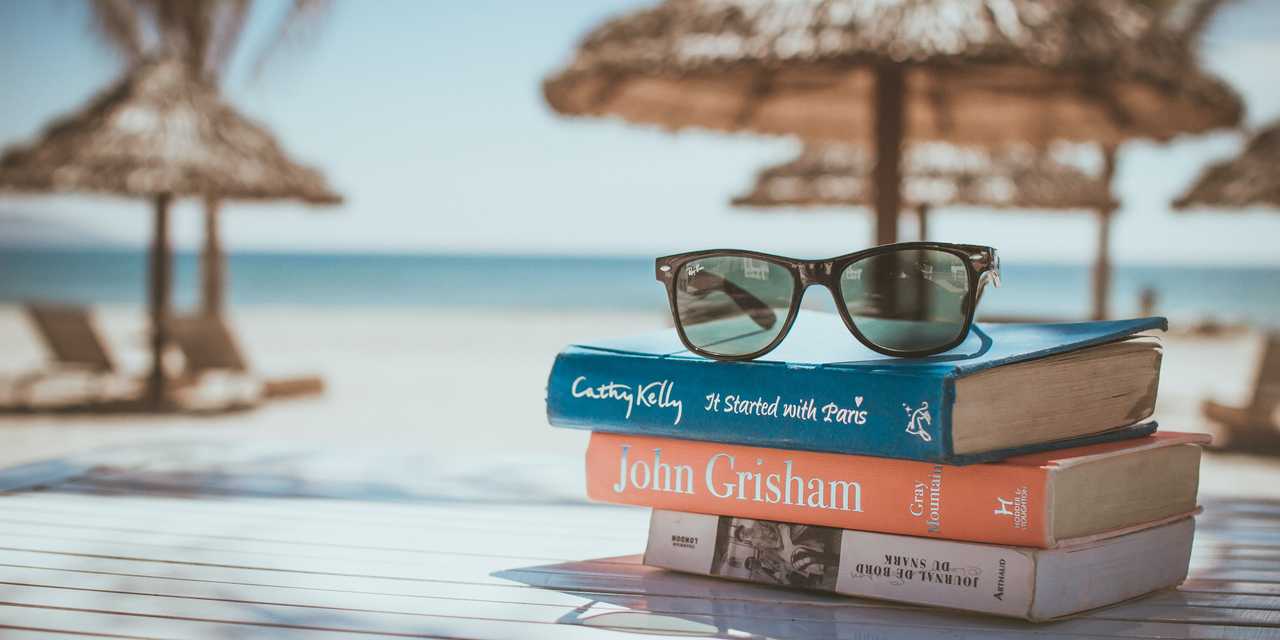Aurinkolasit, kirjapino ja aurinkovarjo rannalla