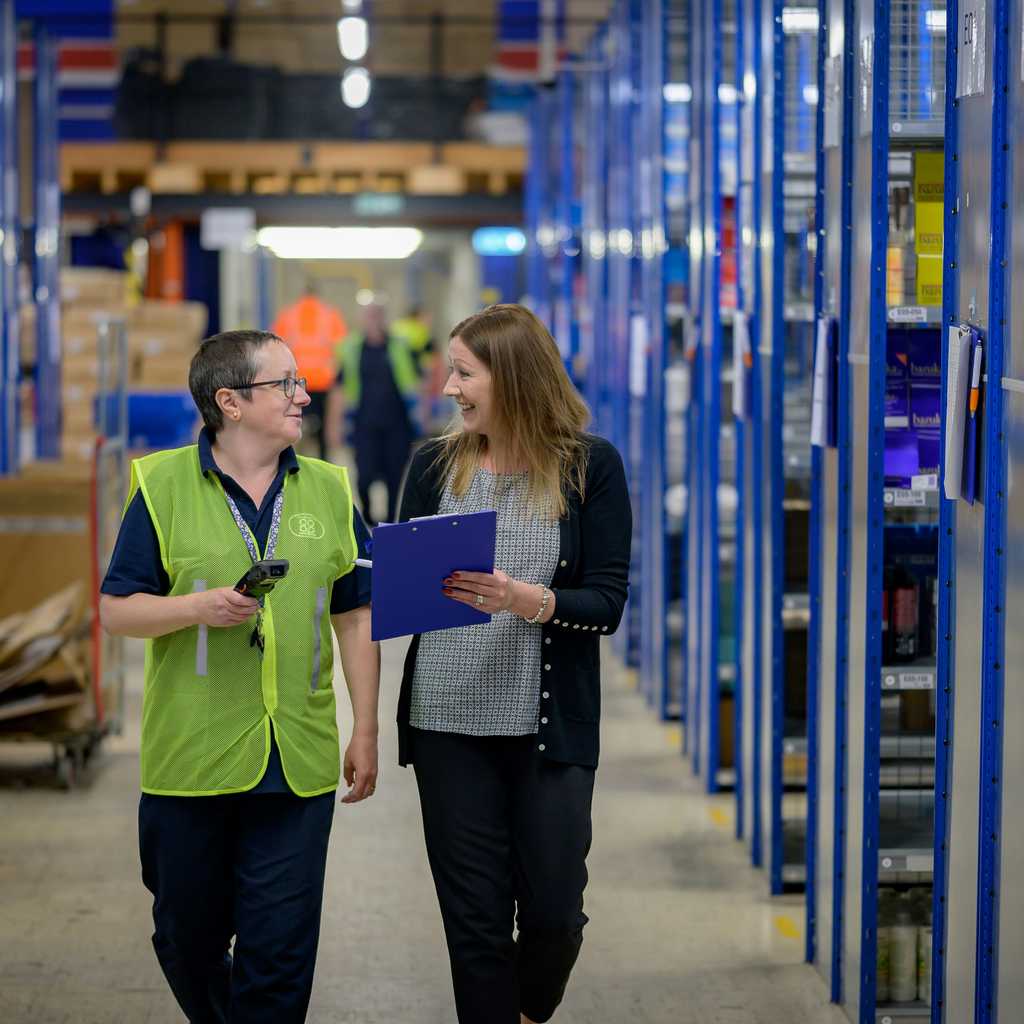 Two people walking in a warehouse between the shelves