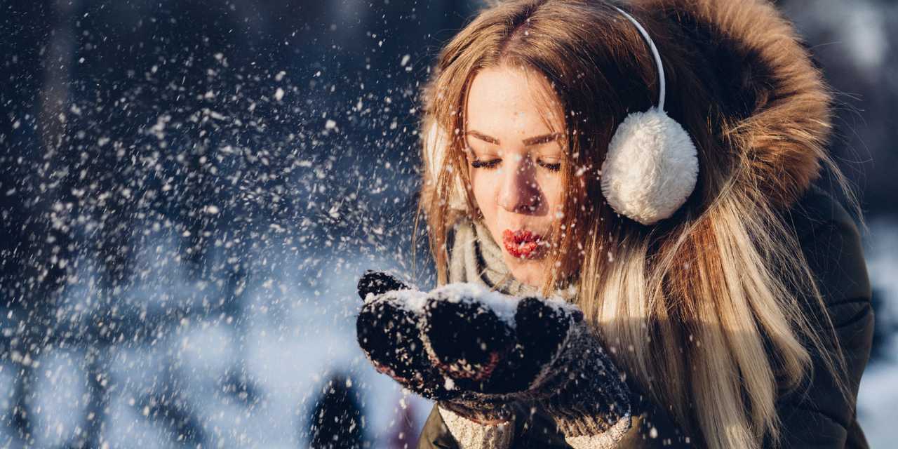 Nainen puhaltaa lunta kämmeneltä