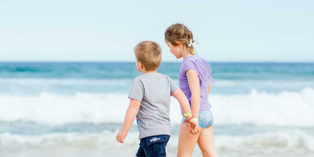 Två barn går hand i hand på stranden
